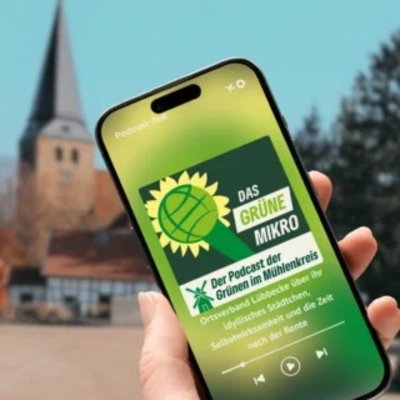 eine Hand hält ein Smartphone, auf dessen Bildschirm die Webseite des Podcast zu sehen ist, im Hintergrund die St. Andreaskirche in Lübbecke